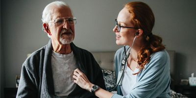 Woman with stethoscope listening to older man's heart