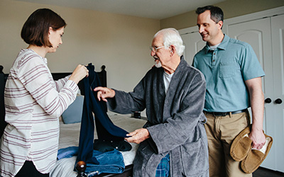 A couple helps an older man choose clothing to put on.