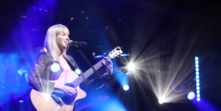 Ashley Campbell sings and plays the guitar onstage, surrounded by blue lighting effects.