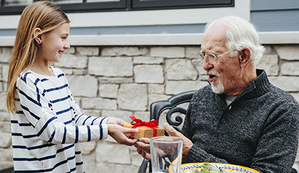 A young girl presents a wrapped gift to her grandfather