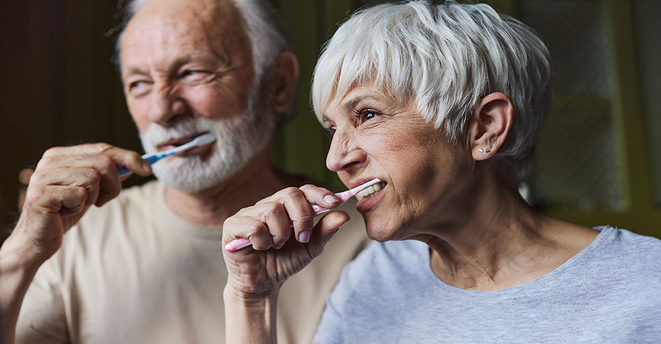 Two older adults brushing their teeth.