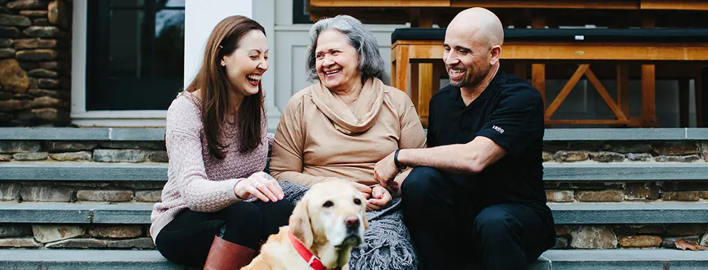 Three people and a golden retriever sitting on porch steps, sharing laughter and connection in Alzheimer’s dementia support.