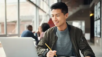Young person smiling while working on a laptop in a shared space, reflecting engagement and independence in Alzheimer’s dementia support.