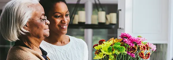 Two people admiring a colorful bouquet indoors, representing moments of joy and connection in Alzheimer’s dementia support.
