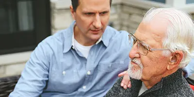 Middle-aged adult offering support to an older adult during a serious conversation, reflecting family care and connection in Alzheimer’s dementia support.