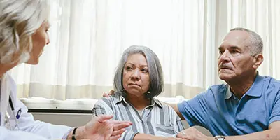 Healthcare professional speaking with two older adults in a clinical setting, highlighting Alzheimer’s dementia consultation and treatment support.
