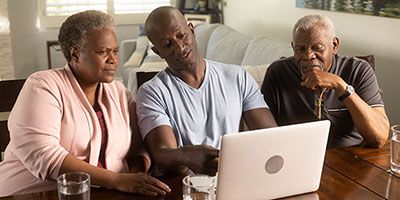 A senior couple uses a laptop with their son.