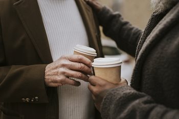two people toasting with coffee outside