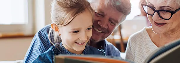 Young girl reading with two older adults, capturing joyful intergenerational connection in Alzheimer’s dementia support.