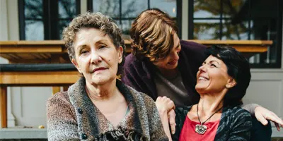 Three adults sitting outdoors, with one looking toward the camera and two sharing a warm moment—capturing interpersonal dynamics in Alzheimer’s dementia support.