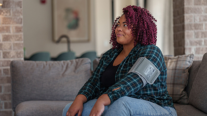 Person sits on a couch with a blood pressure cuff on her arm.