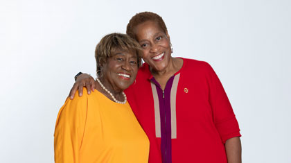 A mother and daughter smile at the camera as they embrace.