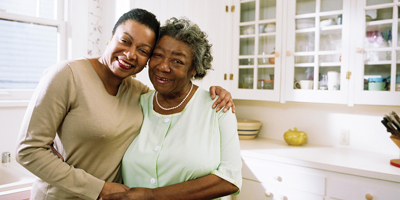 Image of an older Black woman with another Black woman's arms around her shoulders.