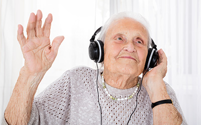 Older woman listening to music through headphones, smiling and with one hand in the air