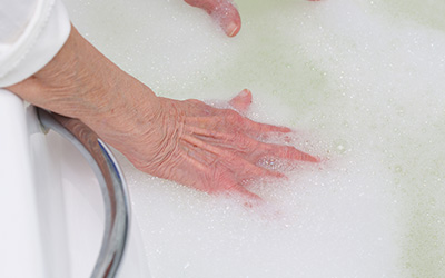A woman testing water temperature with her hand, in a bath with grab rails on the side