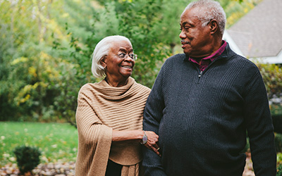Older Black couple walking arm in arm, smiling lovingly at one another