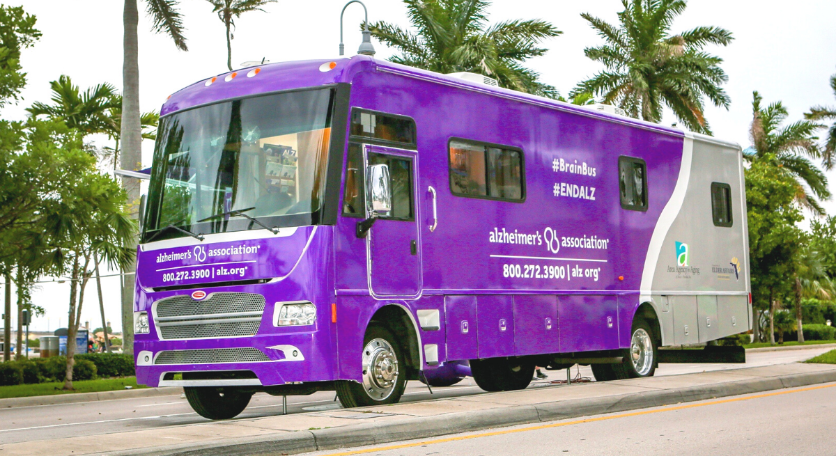 Purple RV with Alzheimer's Association logo parked next to palm trees
